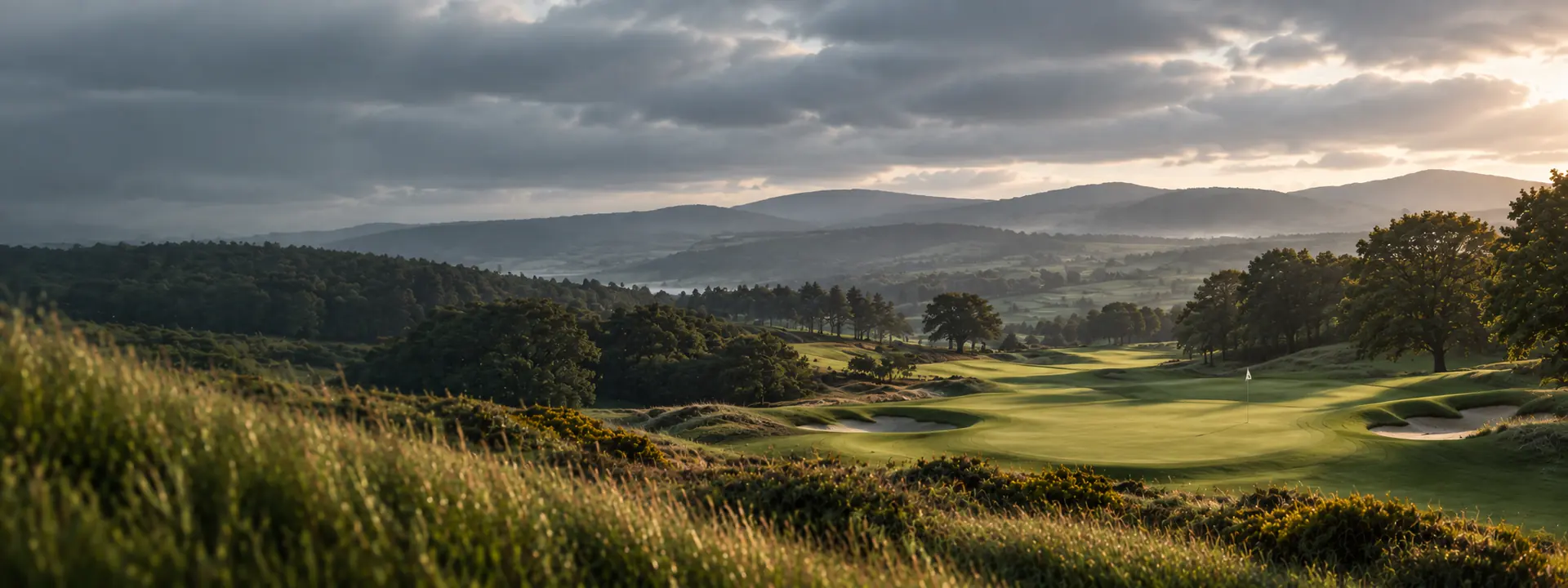 Inland heathland course under soft overcast light, gorse and rough in the foreground and hills fading behind the fairway.